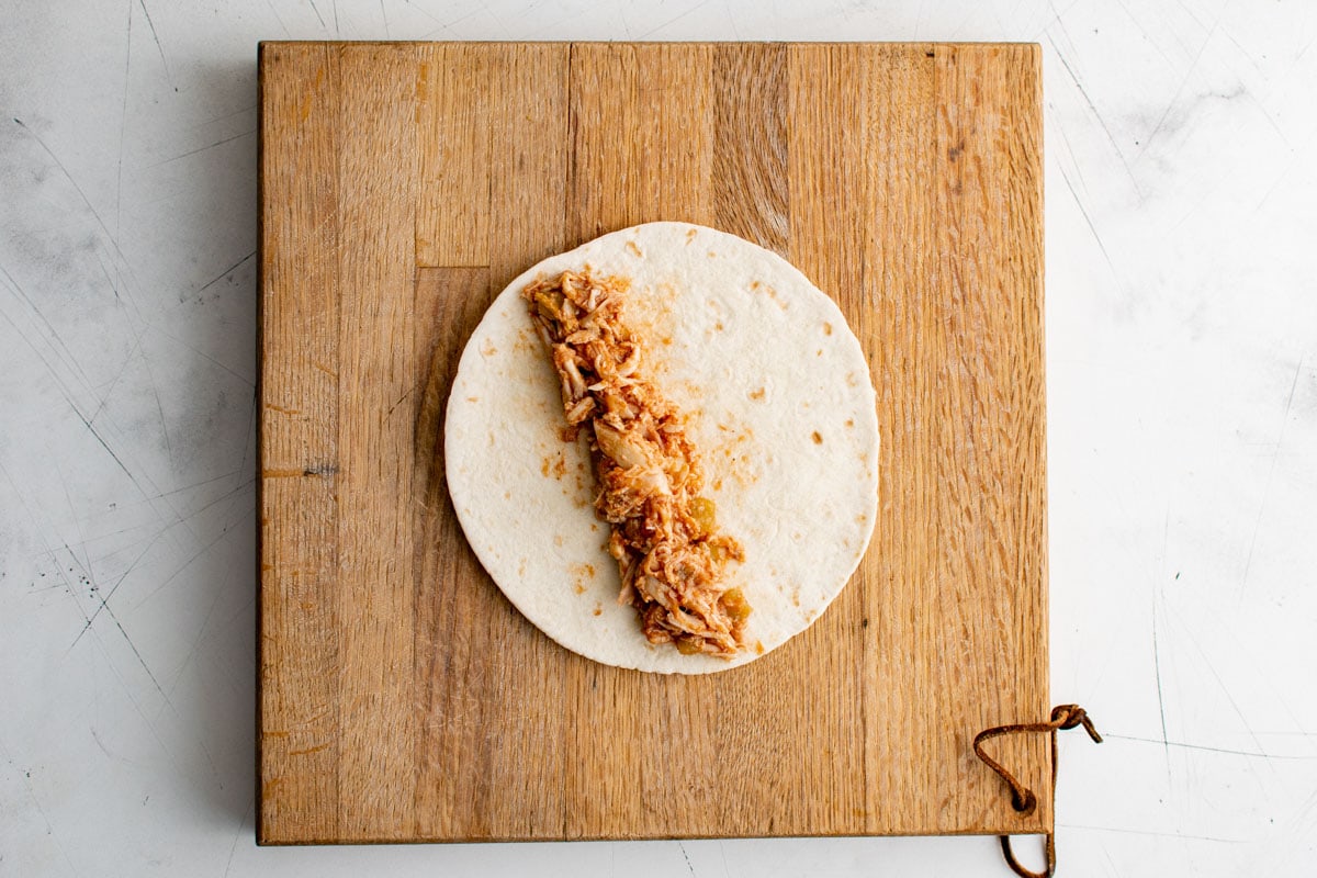 Wooden cutting board, flour tortilla with shredded chicken.