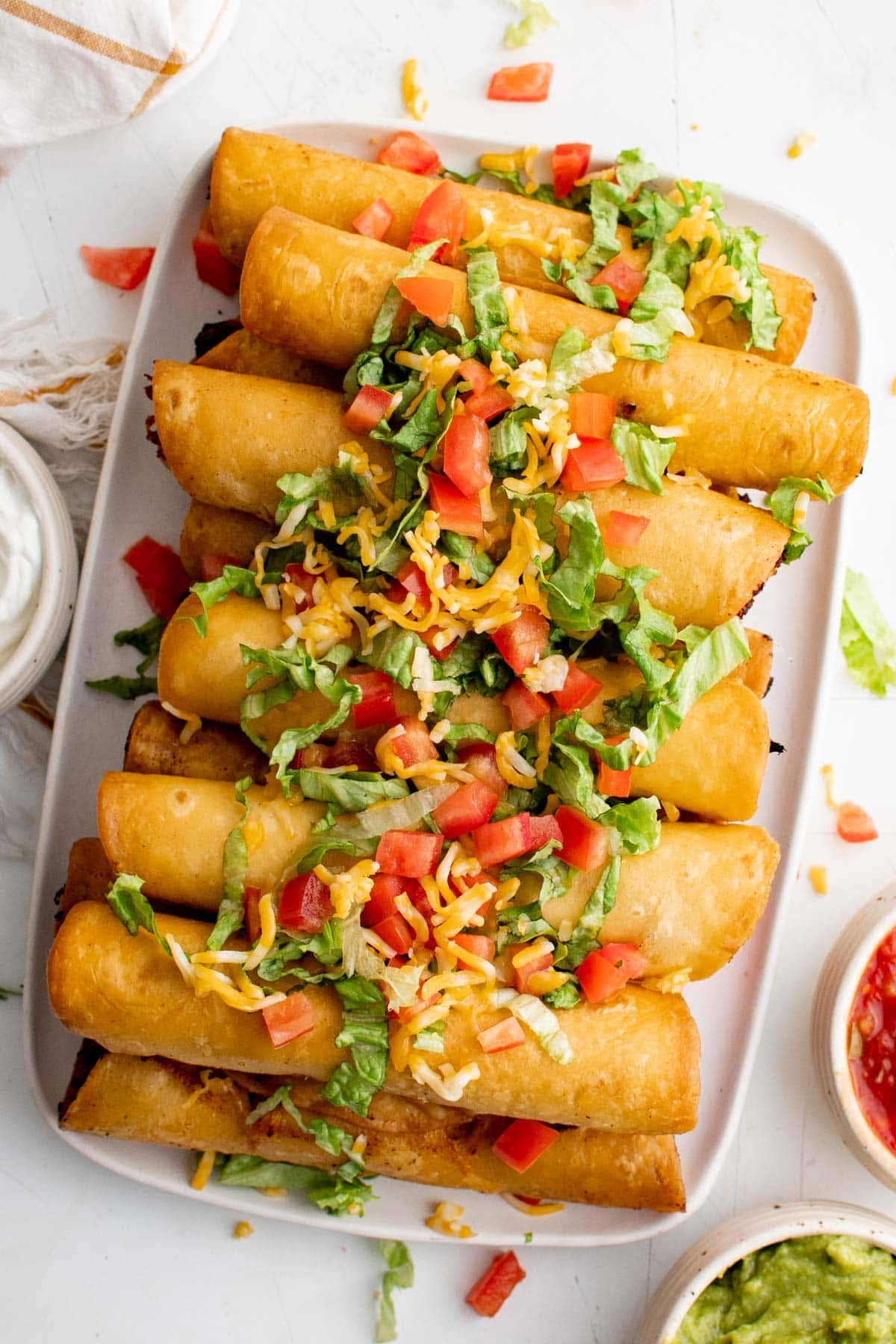 platter of chicken flautas, stacked and topped with tomatoes and shredded lettuces