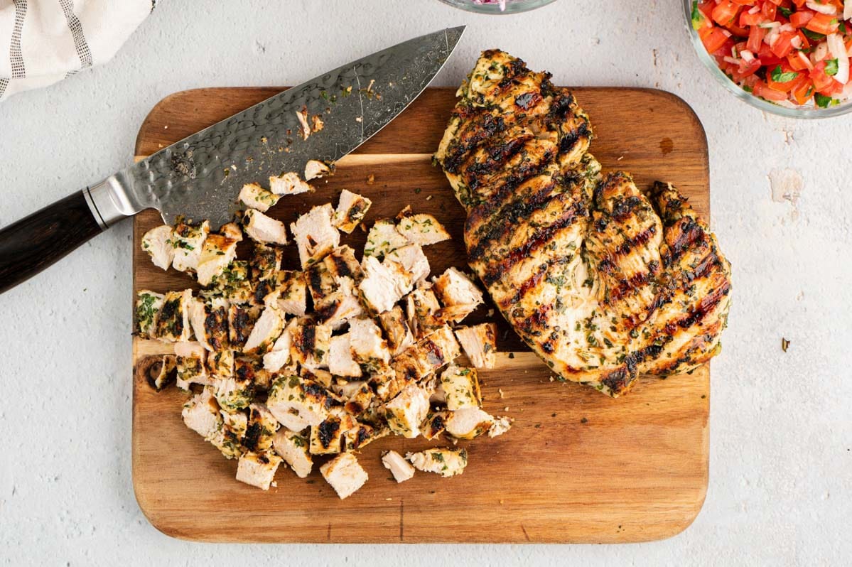 Chopped chicken and a whole chicken breast on a cutting board with a large knife.