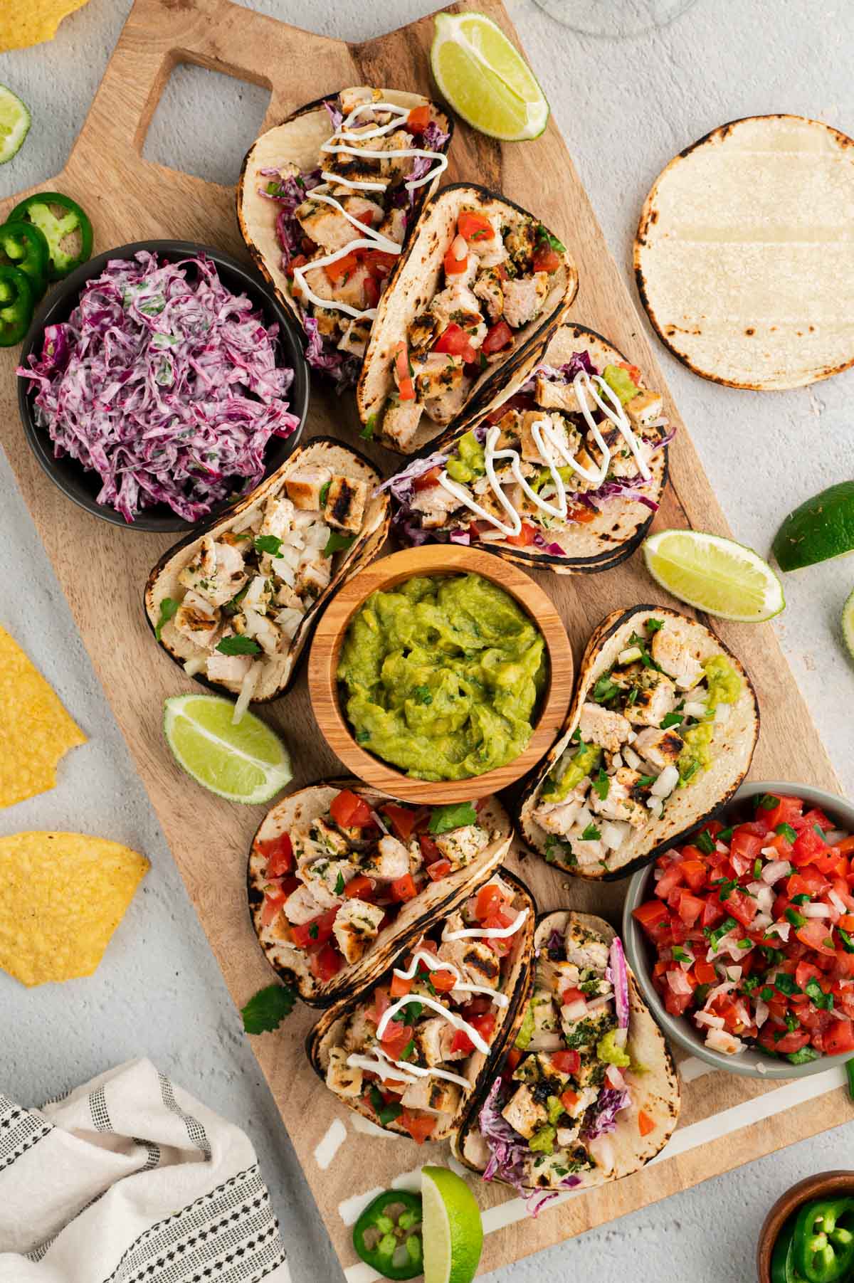 Platter of chicken tacos with various toppings and dish of guacamole. 