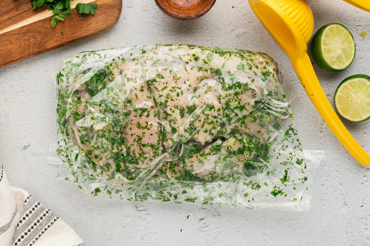 chicken marinating in a plastic bag with lime and cilantro.