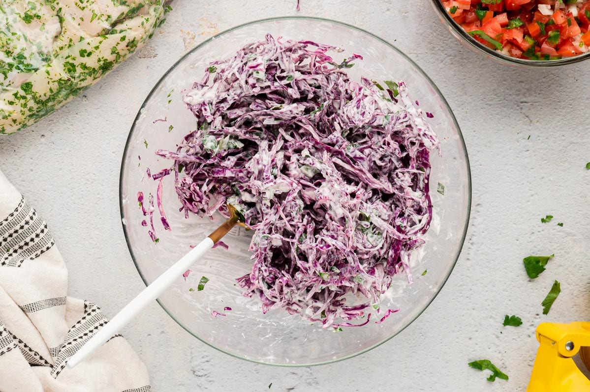 Red cabbage with creamy dressing in a clear glass bowl.