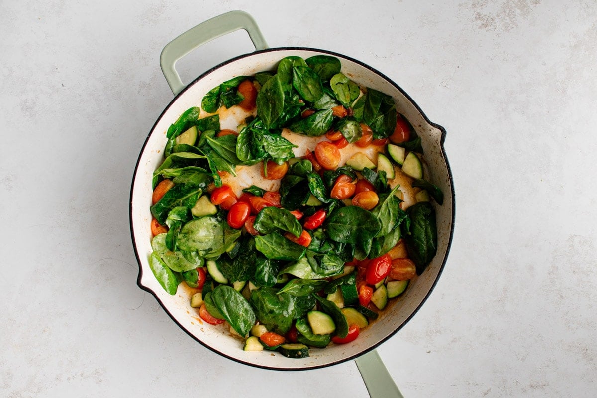 Spinach with sliced tomatoes and zucchini in a skillet.