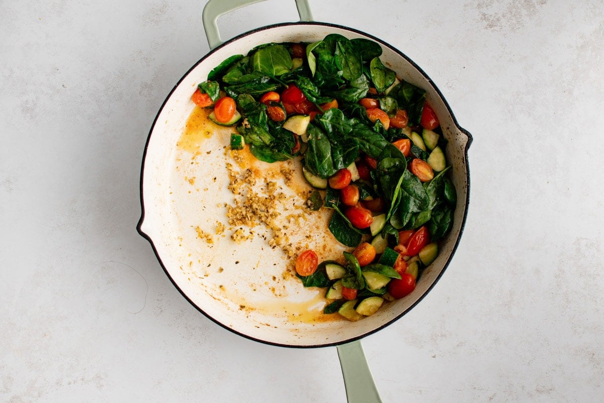 Vegetables pushed aside in the skillet, minced garlic and lemon zest on the other side.