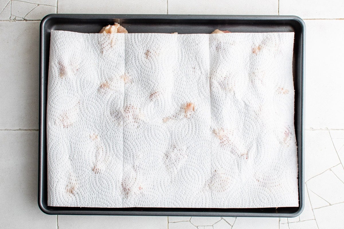 Paper towels placed over the chicken drumettes on the baking sheet.