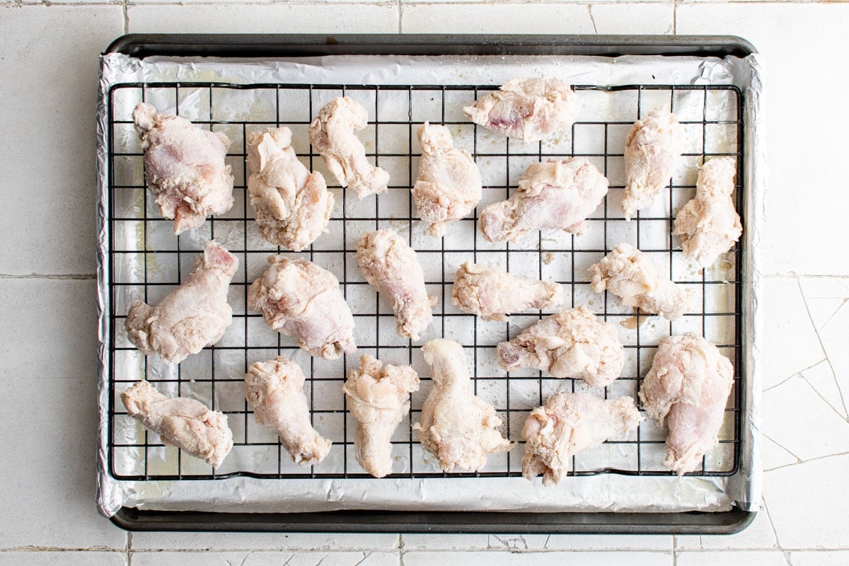 Flour coated chicken wings on a baking rack over a baking sheet.