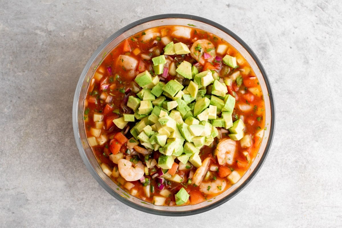 Diced avocado sittin on top of a bowl of mexican shrimp cocktail just before being stirred in.