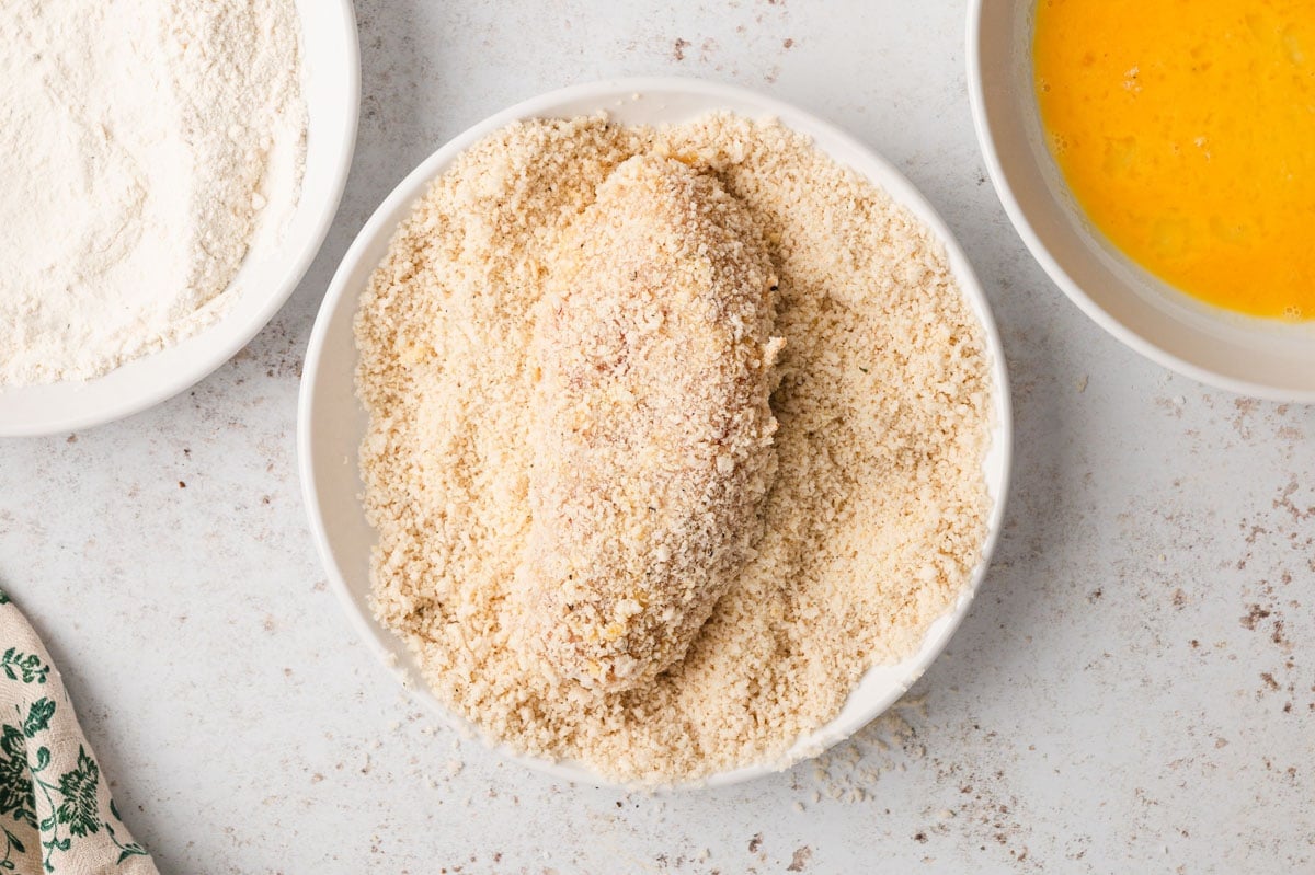 Chicken breast in a dish of breadcrumbs.