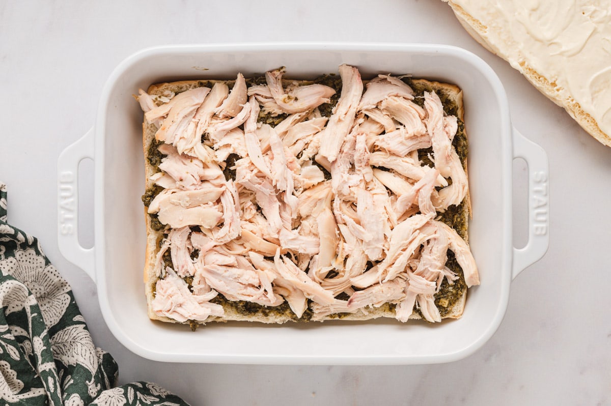 Shredded chicken breast on slider buns in a baking dish.