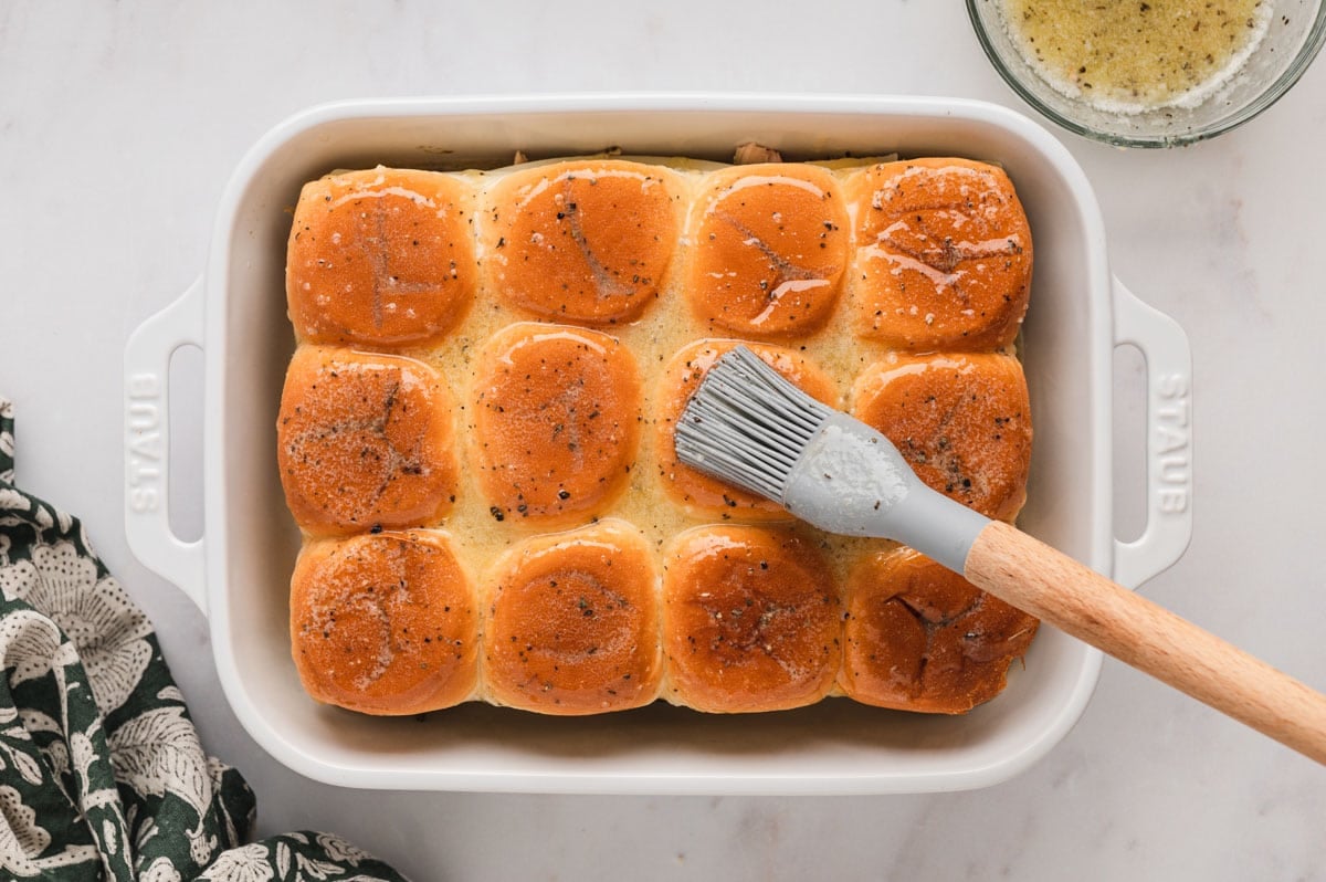 Melted butter brushed on top of slider rolls in a baking dish.