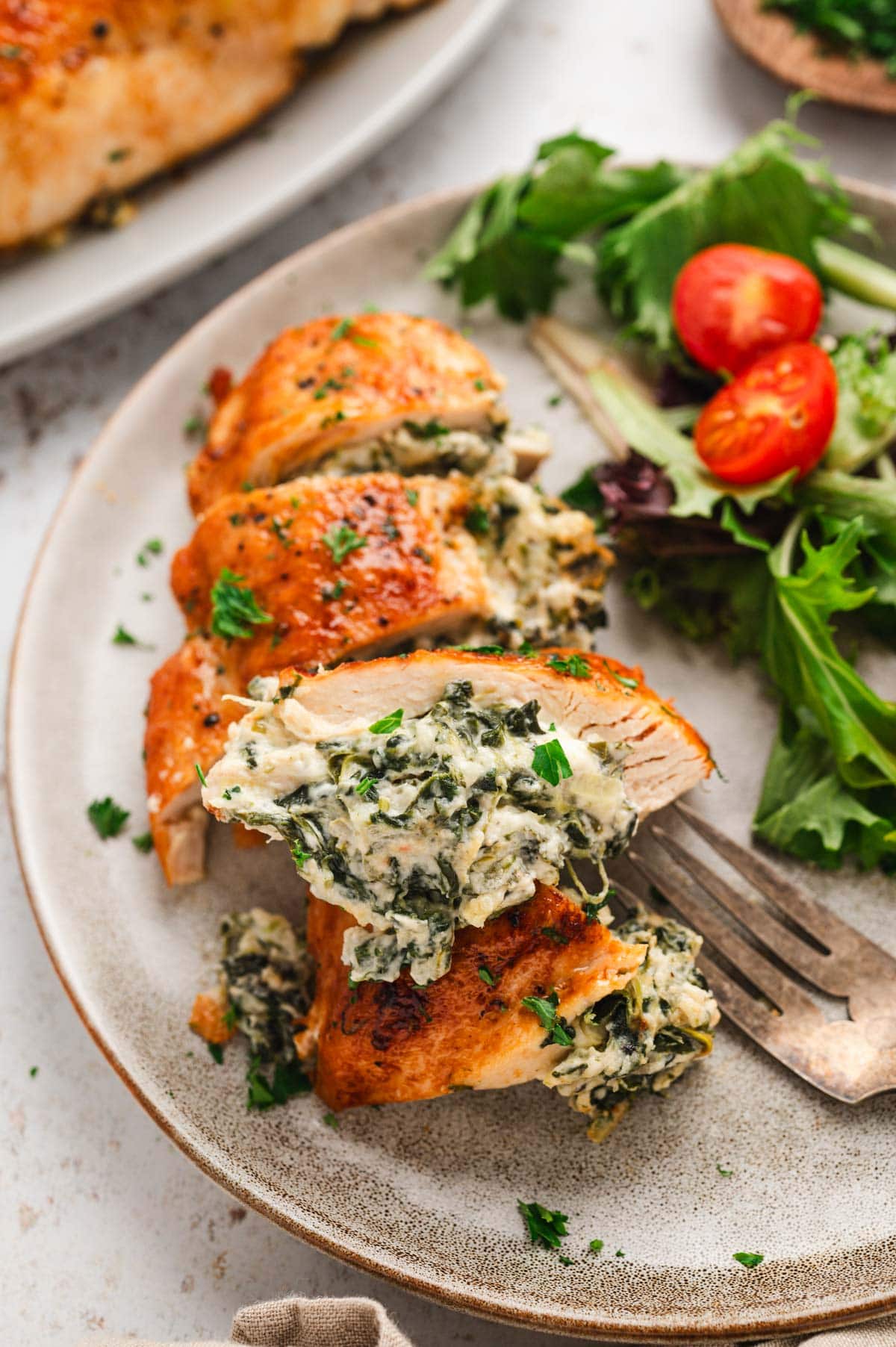 Chicken breast stuffed with cream cheese and spinach, sliced and sitting on a dinner plate with lettuce and tomatoes. 