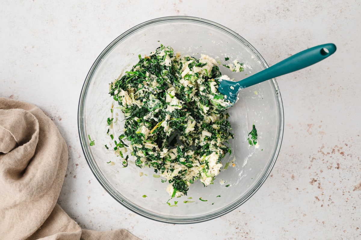 Spinach, cream cheese and cheese mixed together in a clear glass bowl.