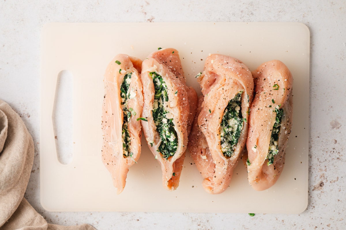 Uncooked chicken breasts on a white cutting board stuffed with cream cheese spinach mixture.