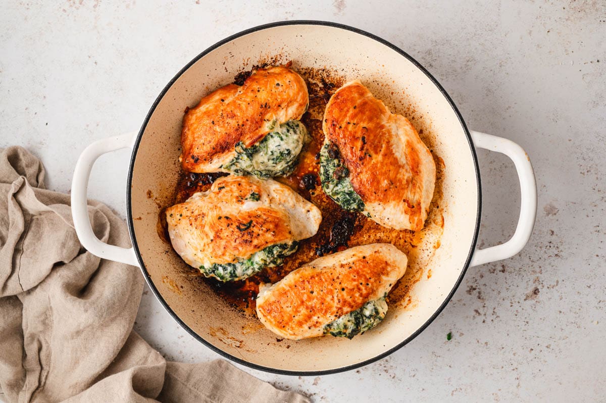 Seared chicken breasts stuffed with cream cheese and spinach in a skillet.