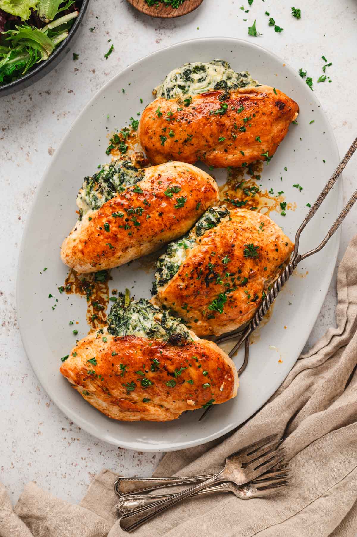White serving platter with 4 seared chicken breasts stuffed with cheesy creamy spinach mixture.