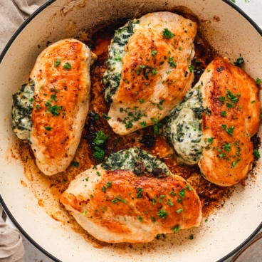 Chicken breasta stuffed with creamy spinach mixture in a skillet.
