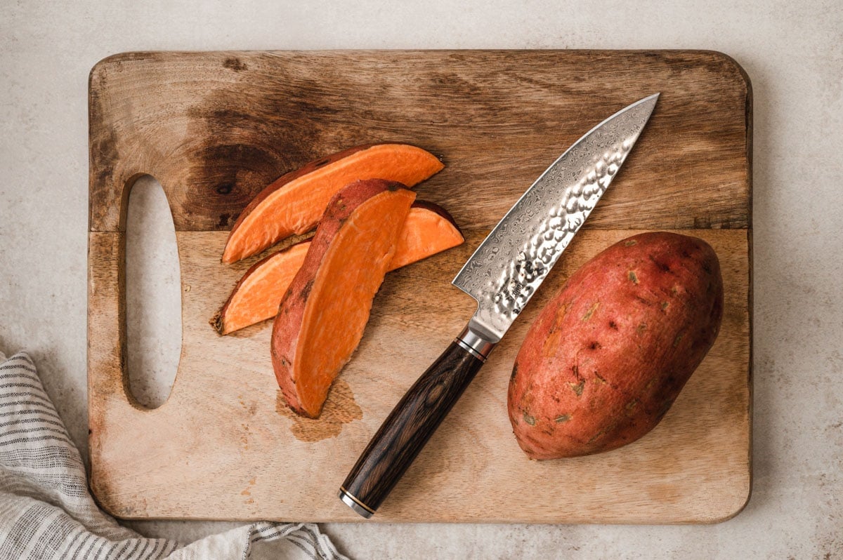Sweet potato and cut wedges on a cutting board with a knife.