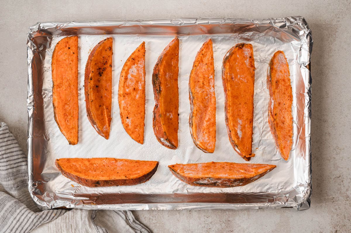 Sweet potato wedges lines up on a foil lined baking sheet.