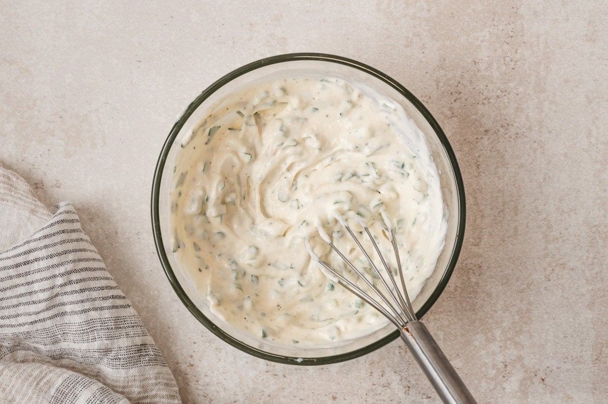 A medium sized clear glass bowl and a small whisk, creamy garlic aioli.