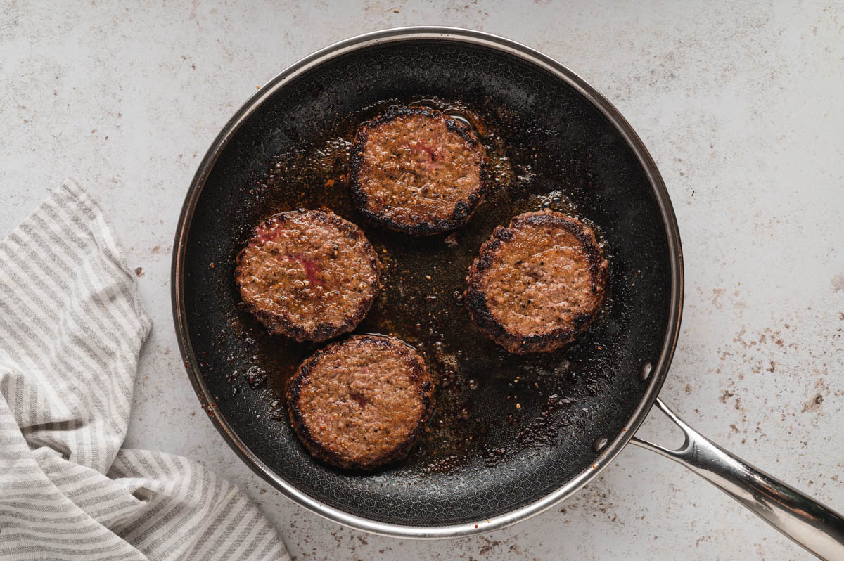 4 hamburger patties frying in a skillet.