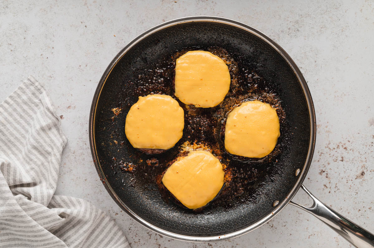 4 hamburger patties with cheese frying in a skillet