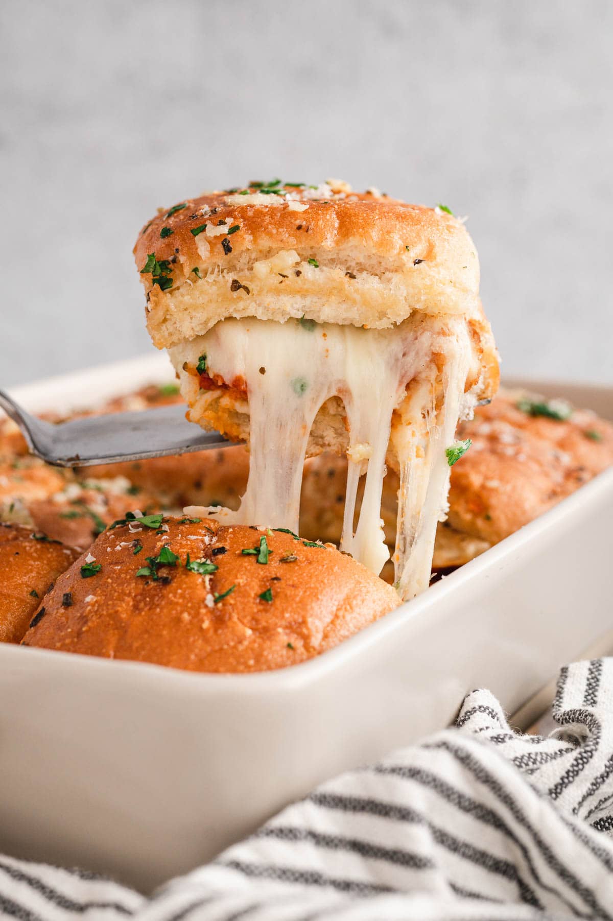 Cheese pull as slider is lifted out of a baking dish.