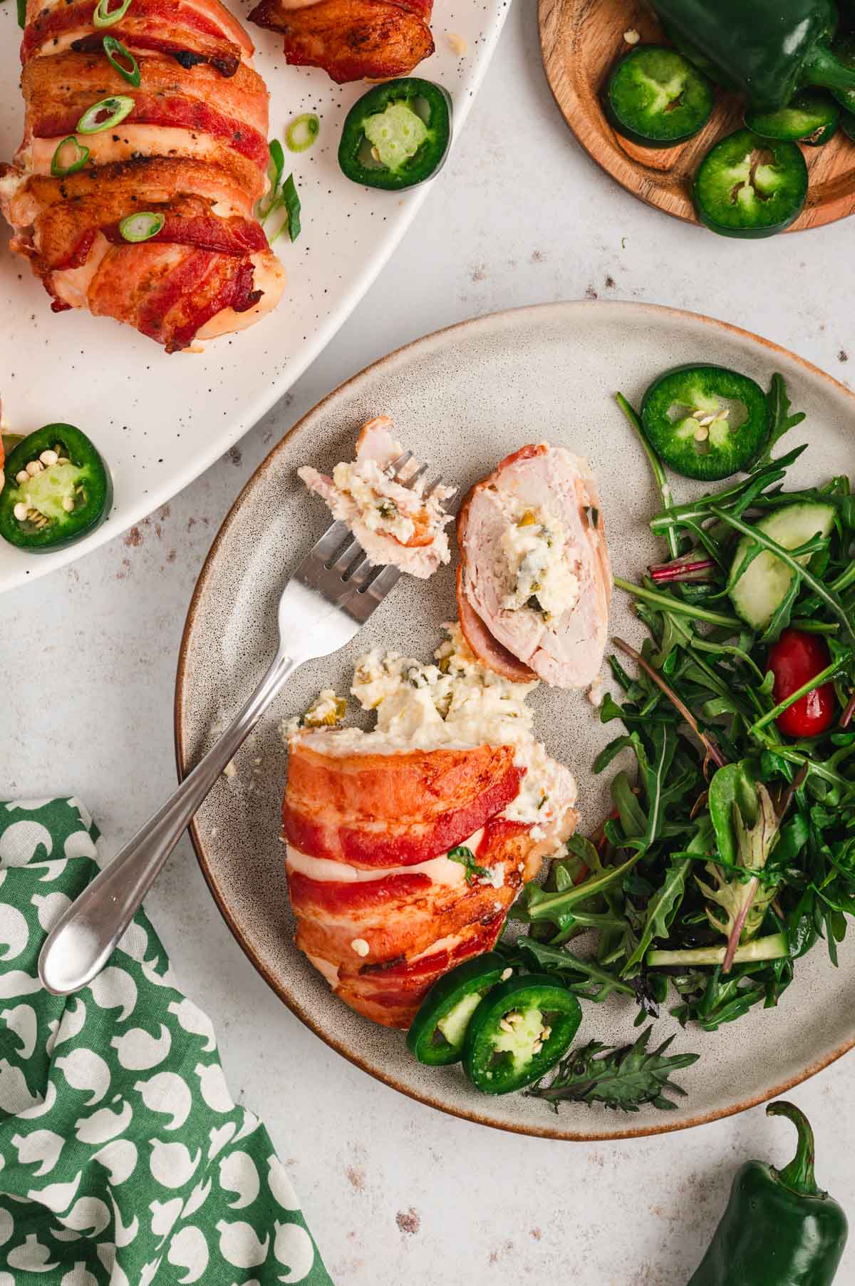 Bacon wrapped, jalapeno and cream cheese stuffed chicken on a plate with greens and a fork.