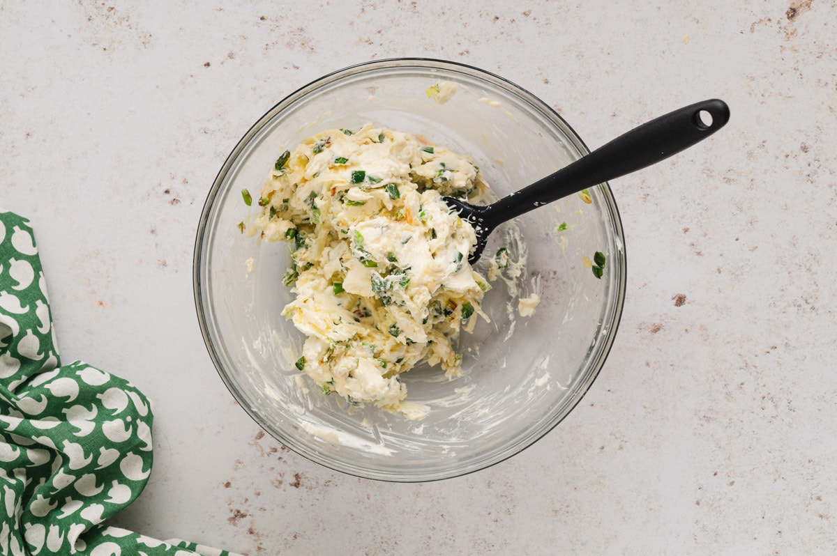 Cream cheese and jalapenos mixed together in a bowl with a spatula.