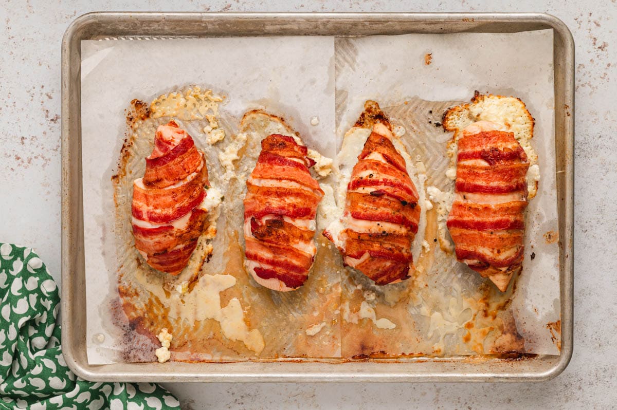 4 chicken breasts wrapped in bacon on a baking sheet.