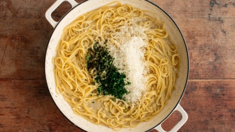 Cooked linguine in a skillet with grated parmesan and fresh parsley and basil.