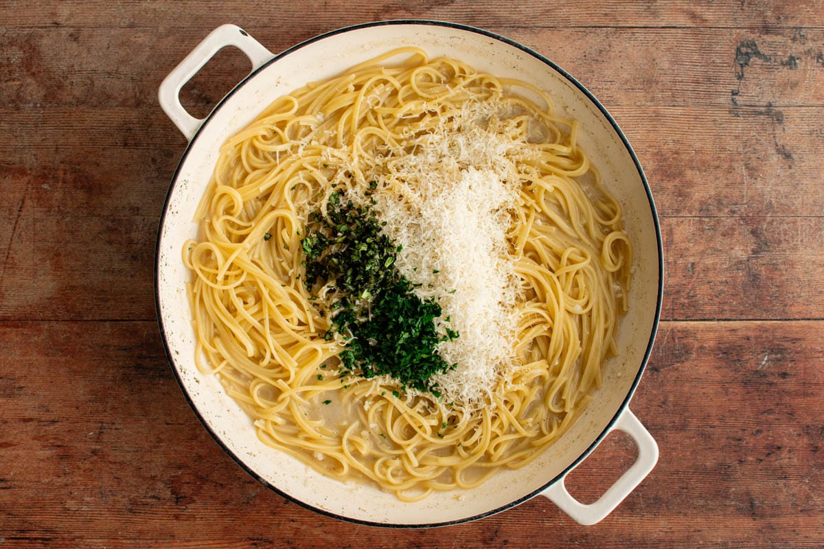 Cooked linguine in a skillet with grated parmesan and fresh parsley and basil.