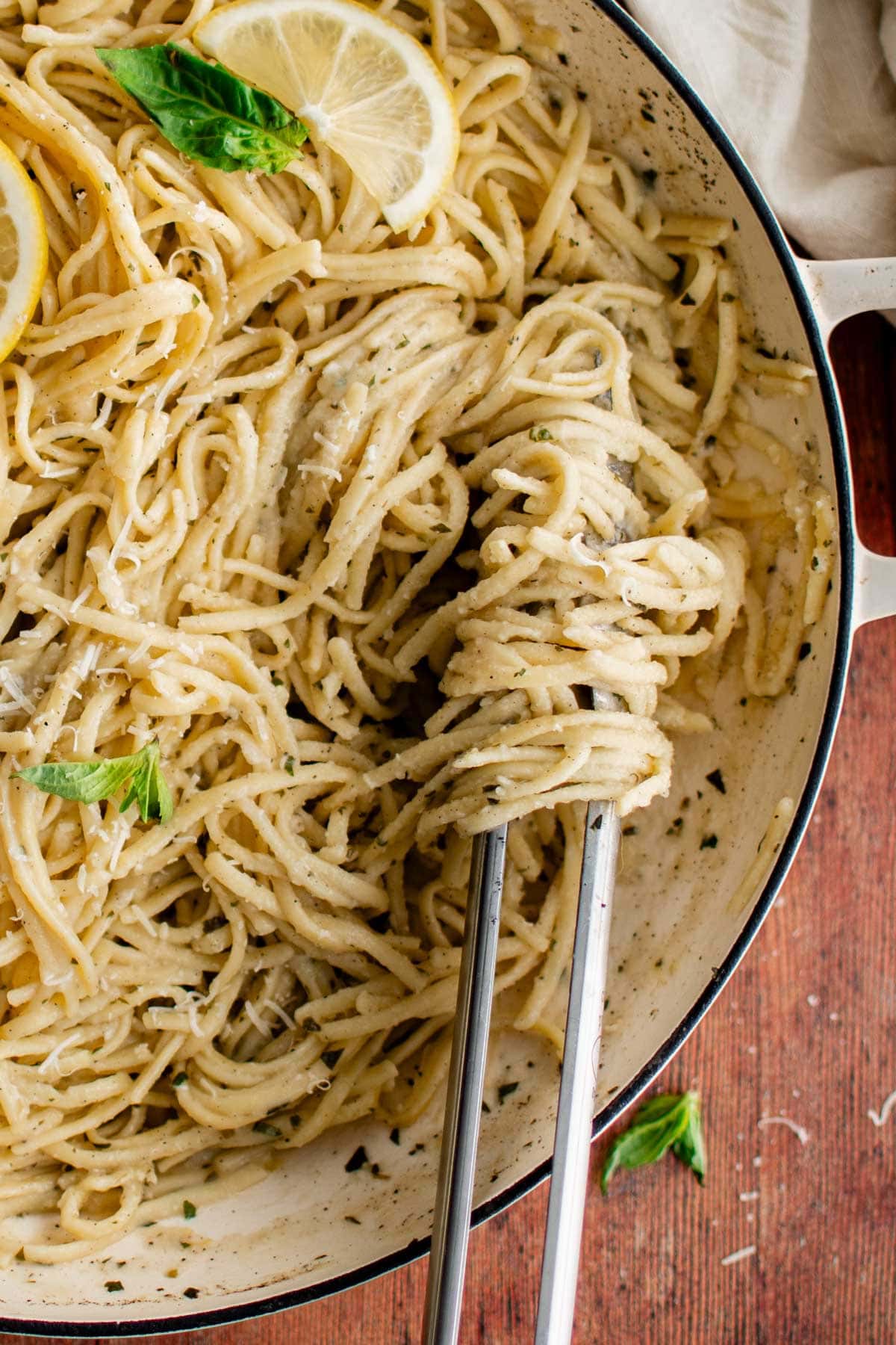 Linguine pasta in a skillet, twirled around a pair of tongs.