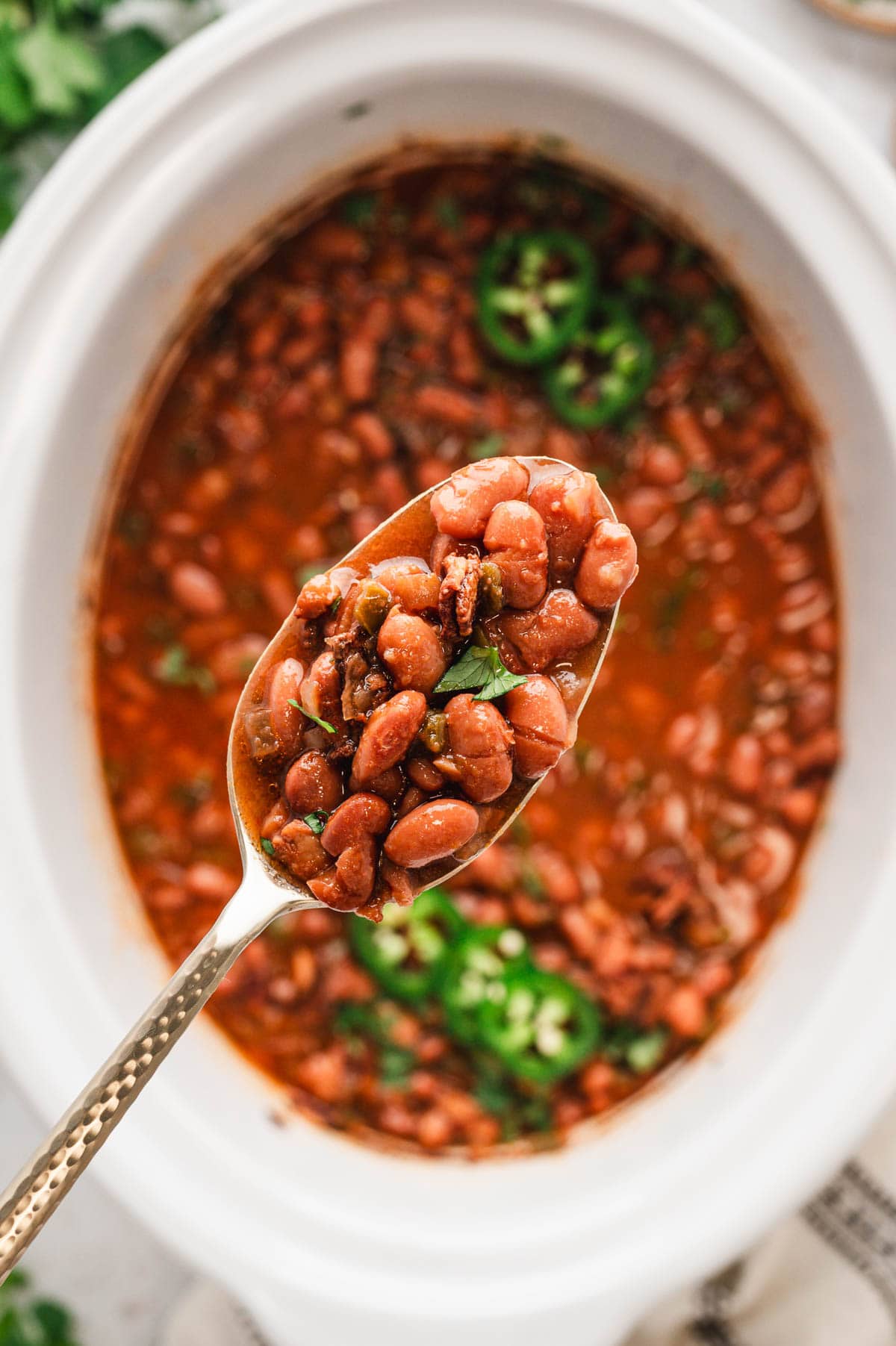 A spoon with beans over a slow cooker full of charro beans.