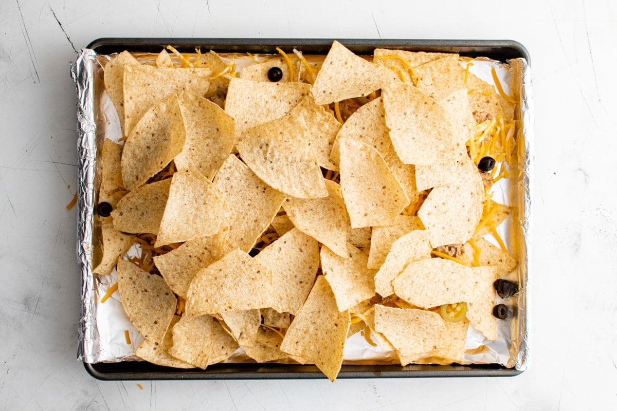 A second layer of tortilla chips on top of nachos on a sheet pan.