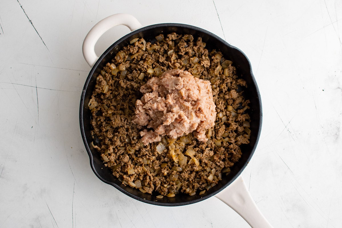 Skillet with cooked ground beef and refried beans.