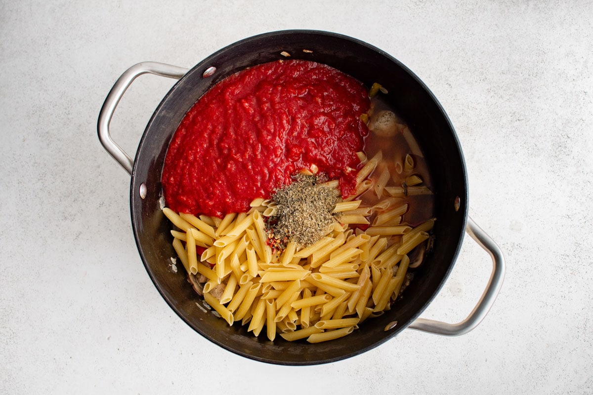 Crushed tomatoes, pasta and seasoning in a large pan.
