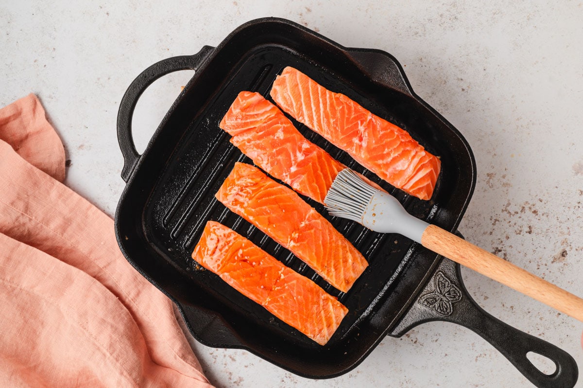 Uncooked salmon in a grill pan with a brush.