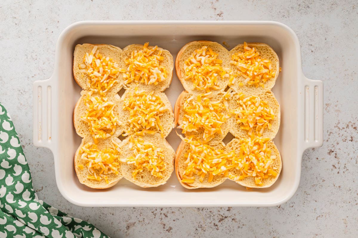 White baking dish with slider buns with shredded cheese.