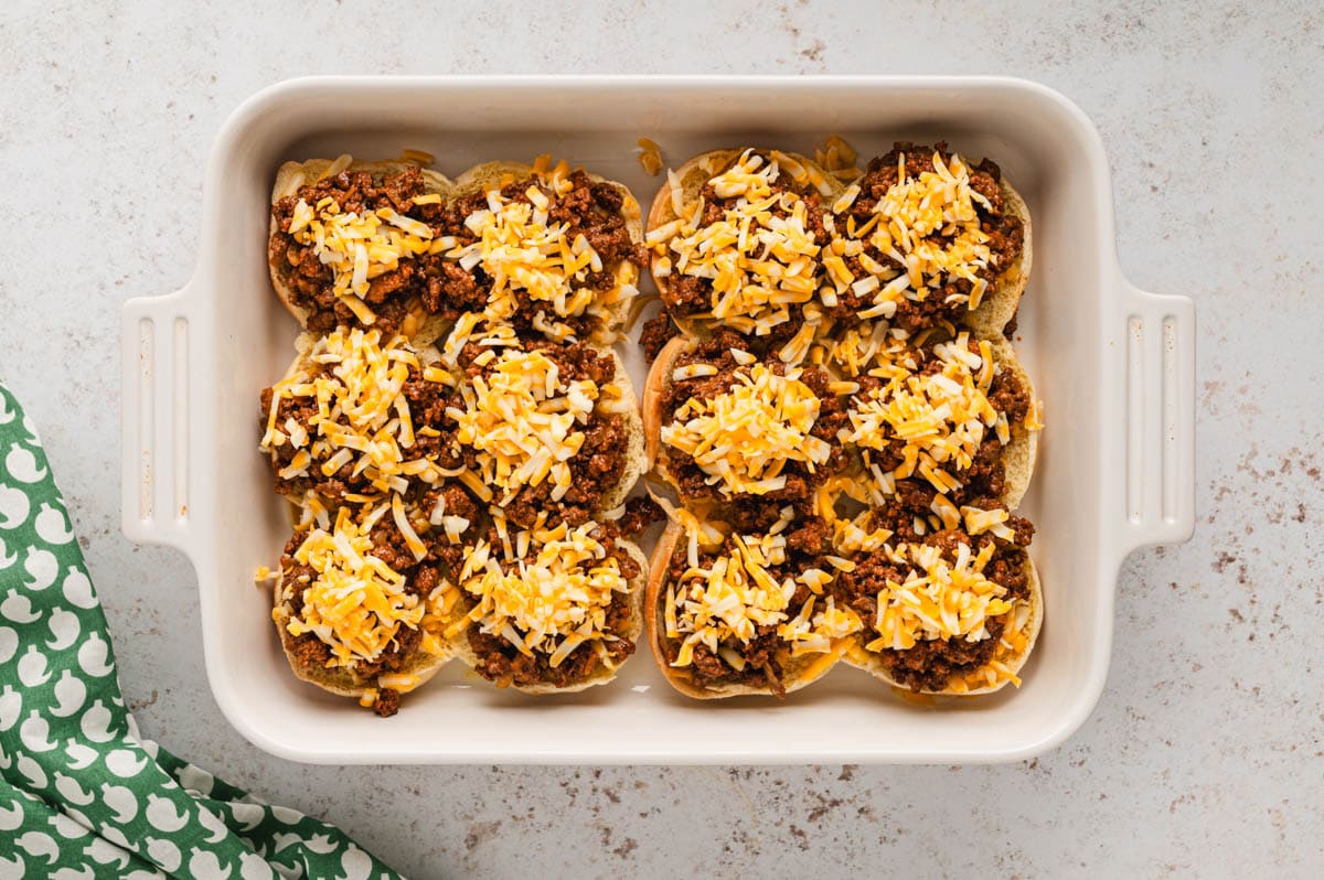 White baking dish with slider buns with shredded cheese and taco meat.