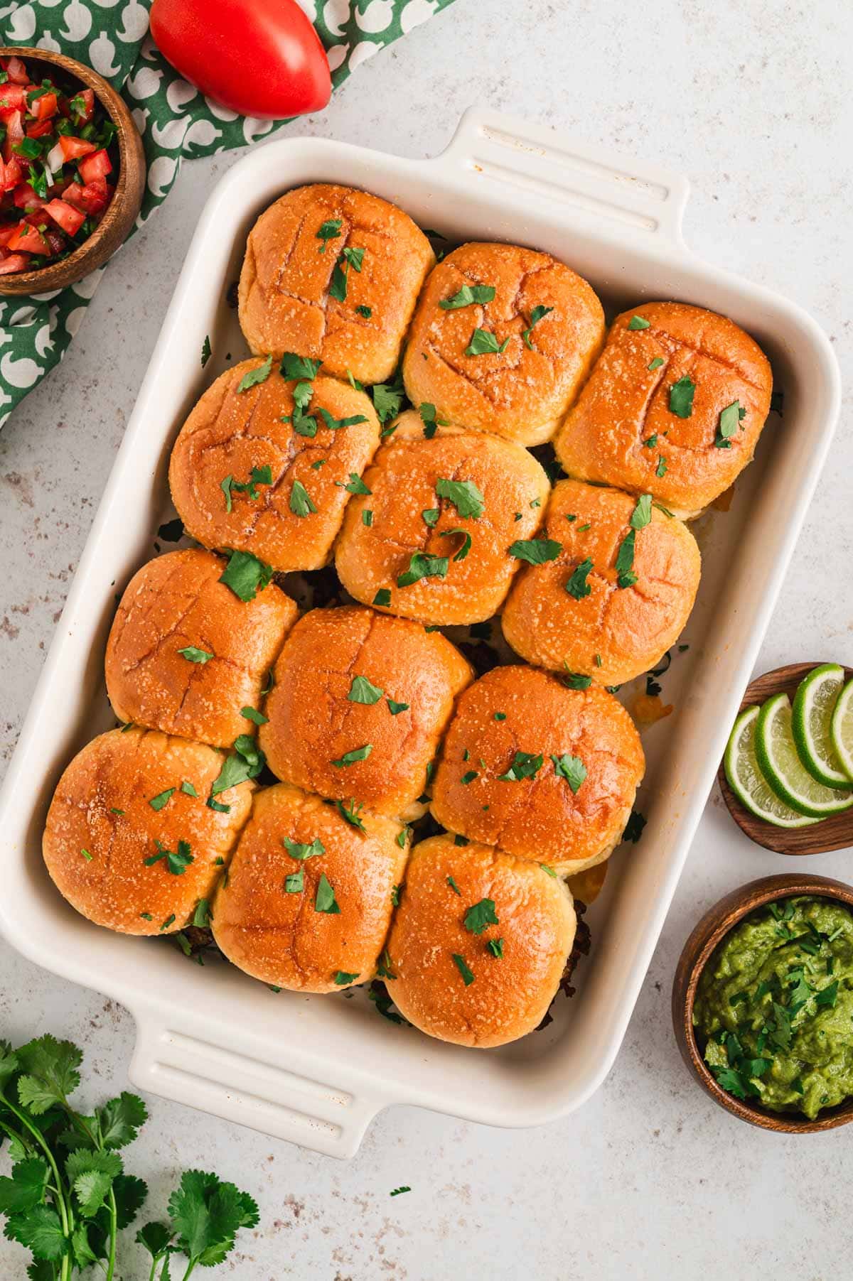 Sliders in a white baking dish topped with chopped cilantro.