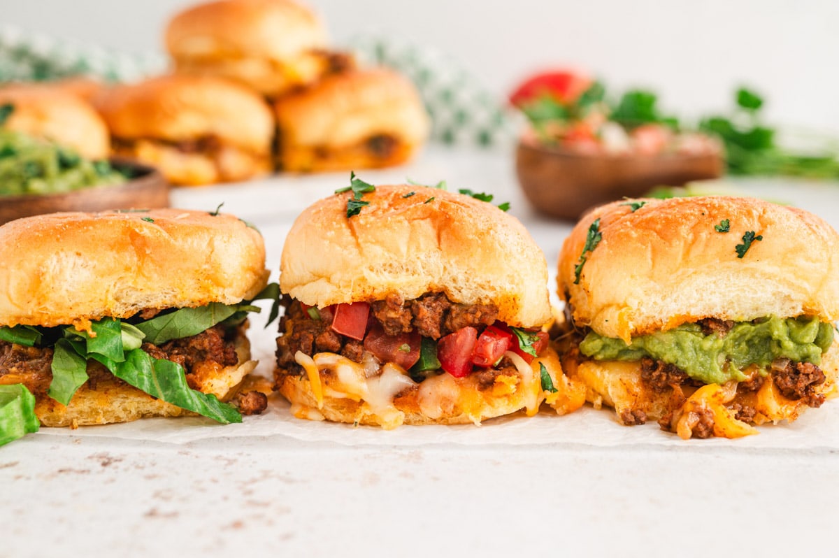 Three sliders side by side, with taco meat, pico de gallo, lettuce and guacamole.