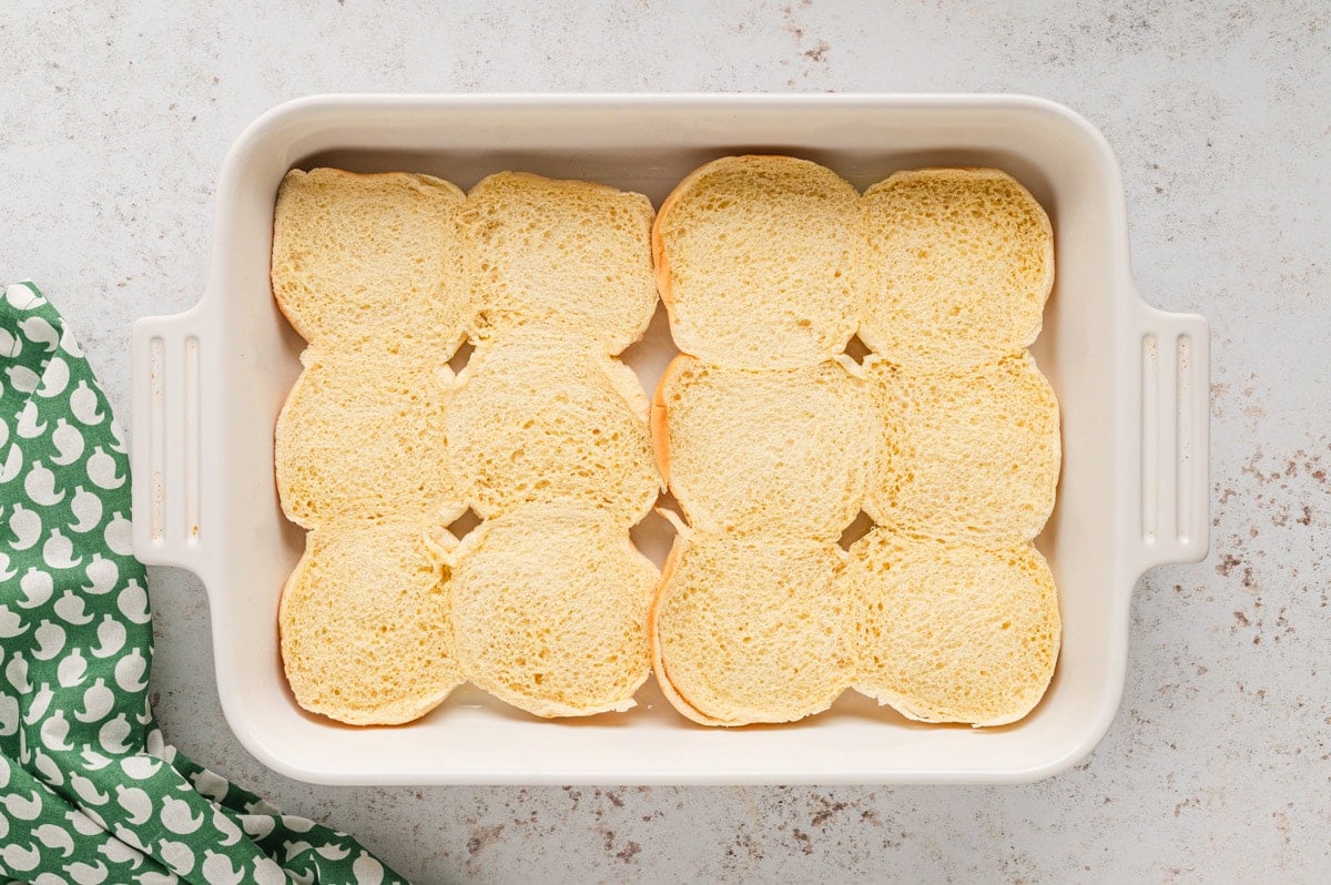 Bottom half of slider rolls in a white baking dish.