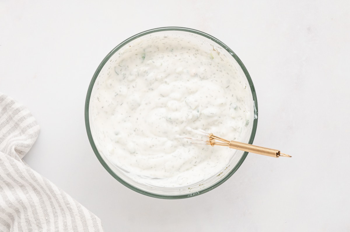 Yogurt sauce in a glass bowl with a spoon.