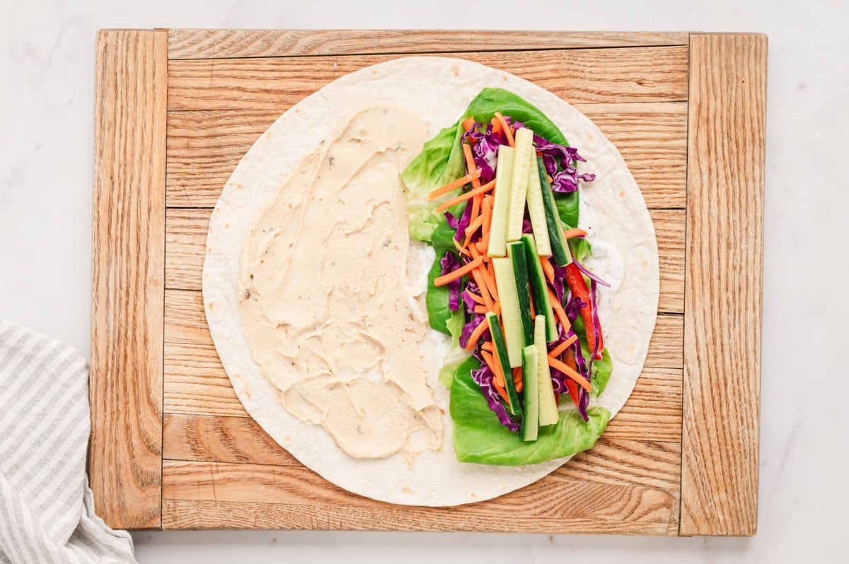 Flat tortilla with hummus on one side and thin vegetable sticks on the other.