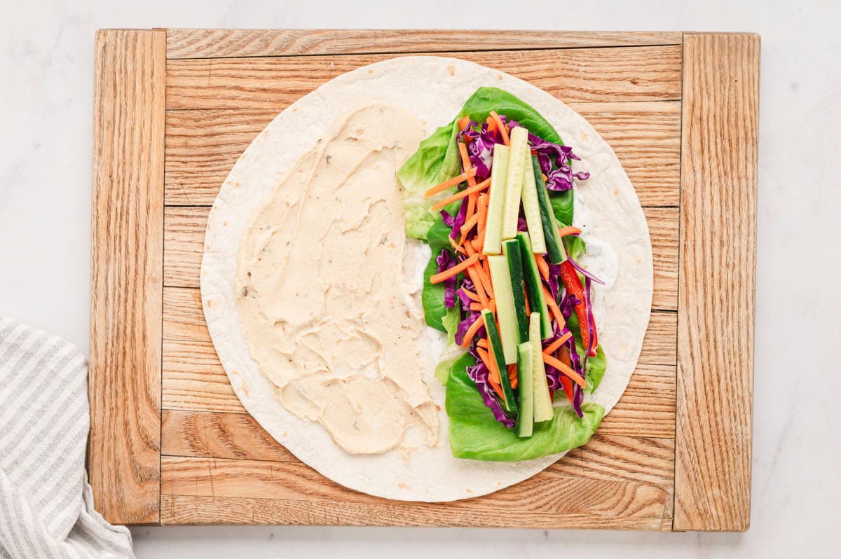 Flat tortilla with hummus on one side and thin vegetable sticks on the other.