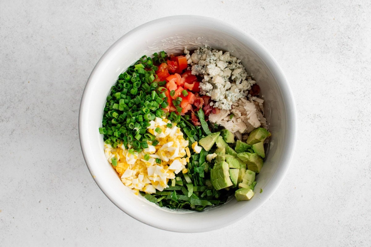 Diced avocado, diced tomato, chopped hard boiled eggs, green onions, chopped chicken in a bowl.