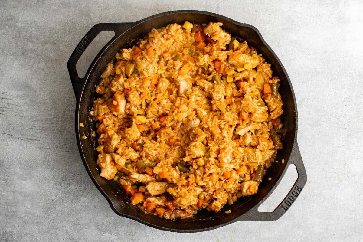 Cooked chicken, vegetables and rice in a cast iron skillet all mixed together.