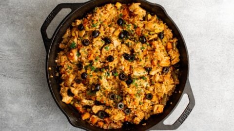 Cooked chicken, vegetables and rice in a cast iron skillet topped with sliced olives.