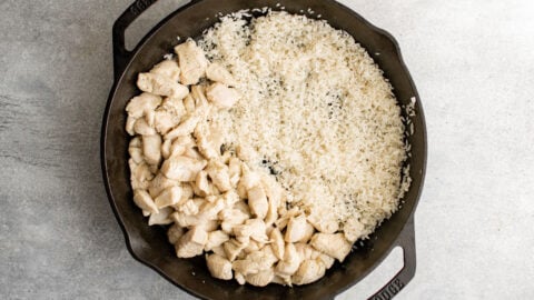 A cast iron skillet with cooked diced chicken breasts in one side and white rice on the other.