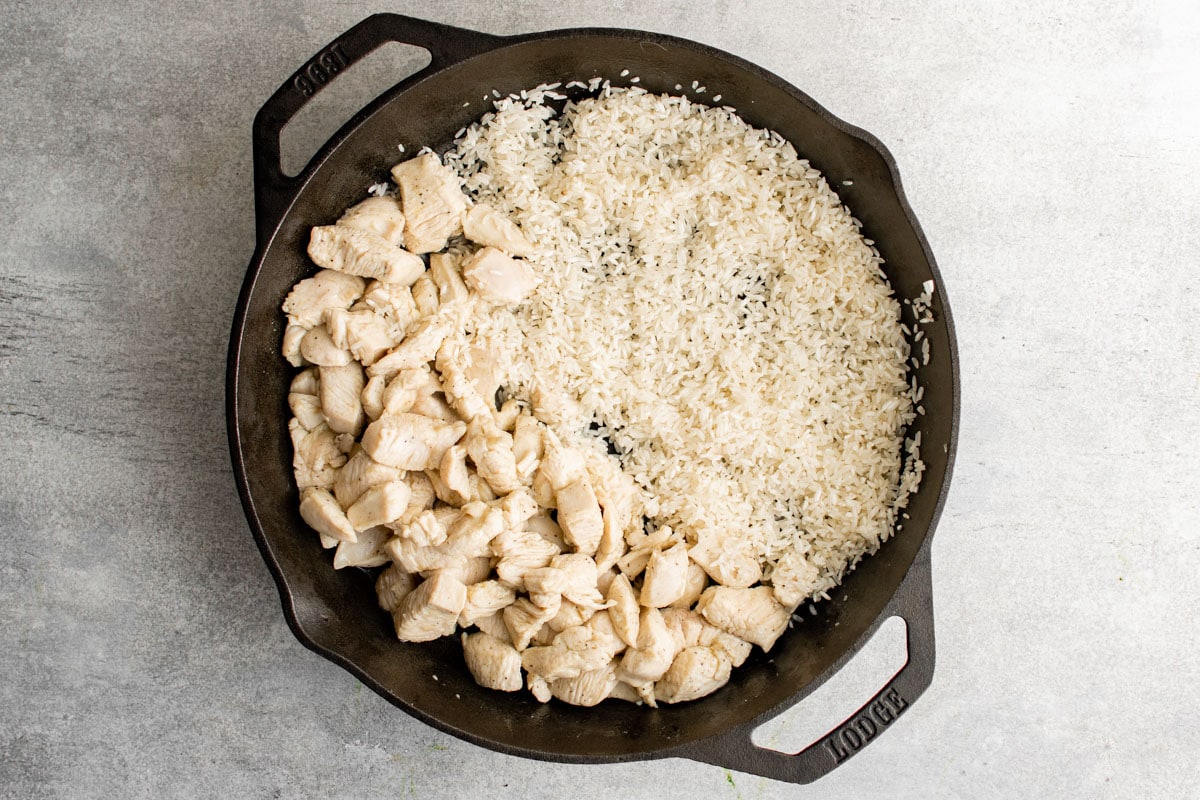 A cast iron skillet with cooked diced chicken breasts in one side and white rice on the other.